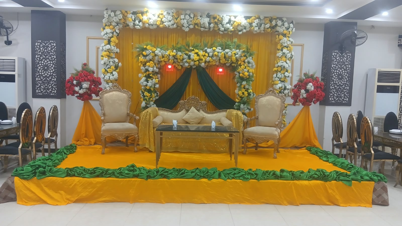 Yellow and green mehndi stage with floral arch at Rawal Wedding Palace